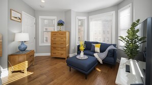 A living room with a sofa, ottoman, wooden dresser, and a TV stand. - Modern North End Studio (Boston)