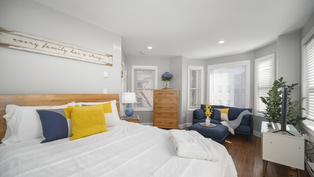A modern bedroom with a large bed, a blue sofa, and a wooden dresser. - Modern North End Studio (Boston)
