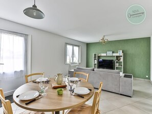 A dining area with a round table set for four, a grey sofa, a TV, and a green accent wall.