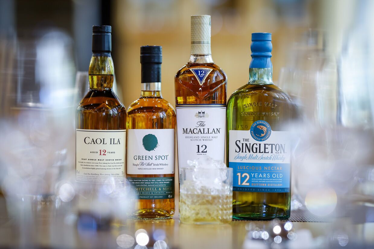 Cuatro botellas de whisky sobre una superficie reflectante.