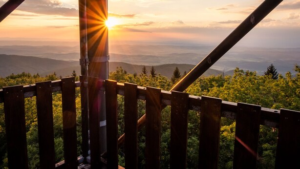 Barandilla de madera con vistas a un paisaje montañoso y un atardecer de fondo.
