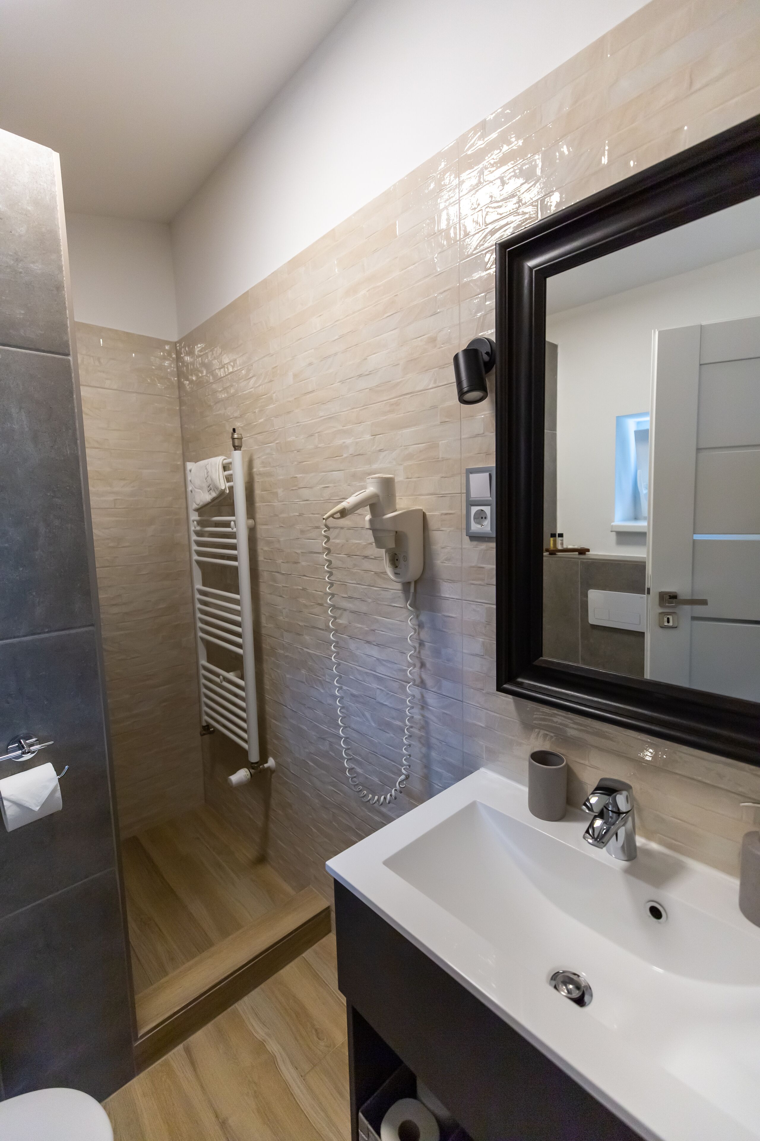Une salle de bain avec un lavabo blanc, un miroir, un porte-serviettes et un espace douche.