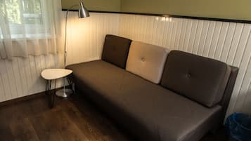 A room with a brown sofa, a small round table, a lamp, and a trash bin.