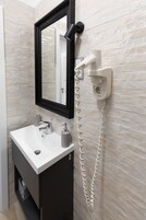 Un baño con un lavabo blanco, un mueble negro, un espejo y un secador de pelo conectado a un enchufe.