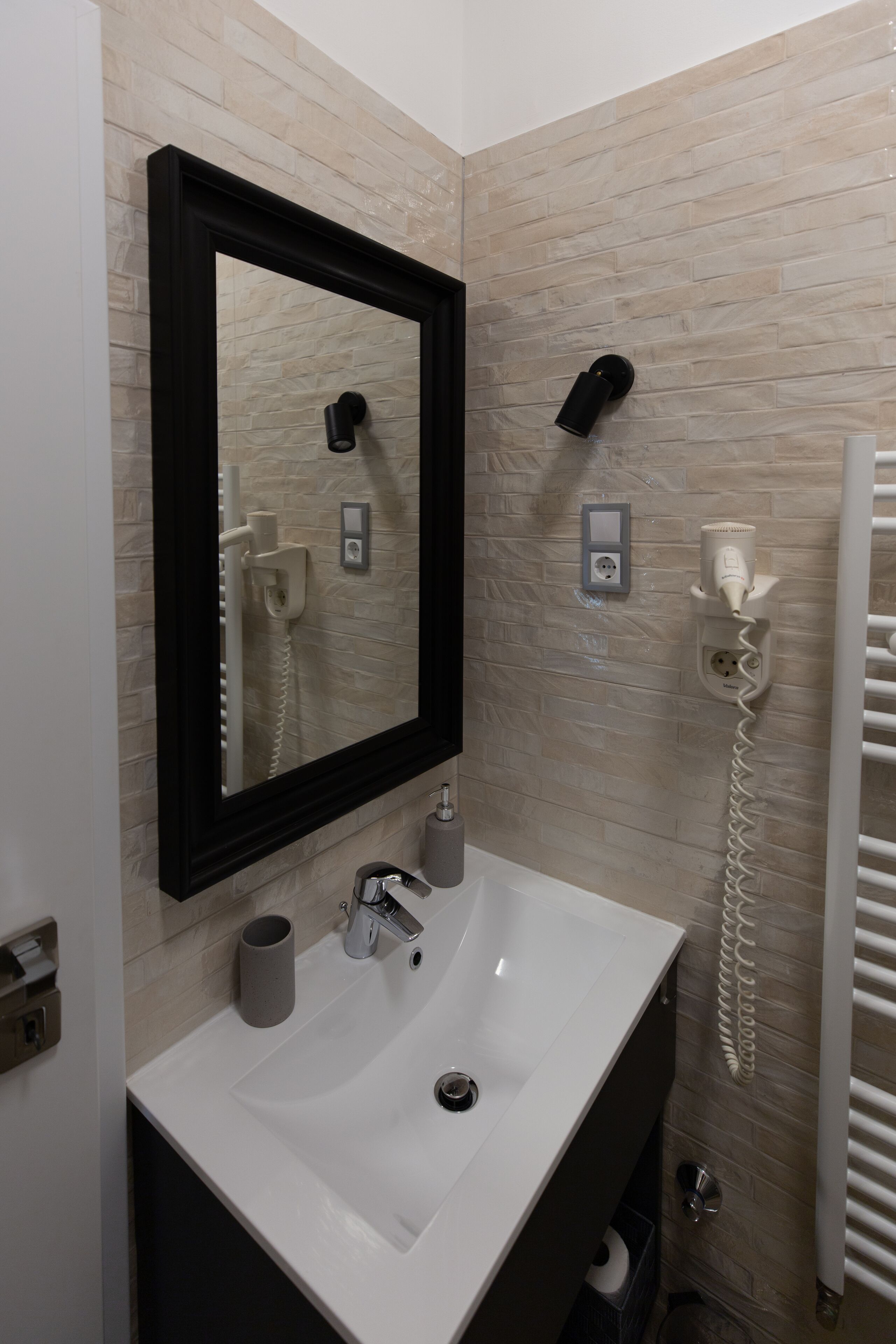 Un baño con lavamanos blanco, espejo, secador de pelo y toallero.