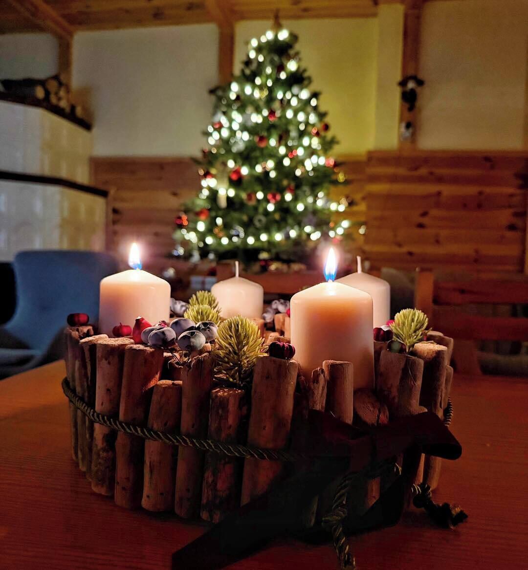 Et hyggeligt rum med træpaneler, et juletræ og tre tændte stearinlys på en træsokkel.