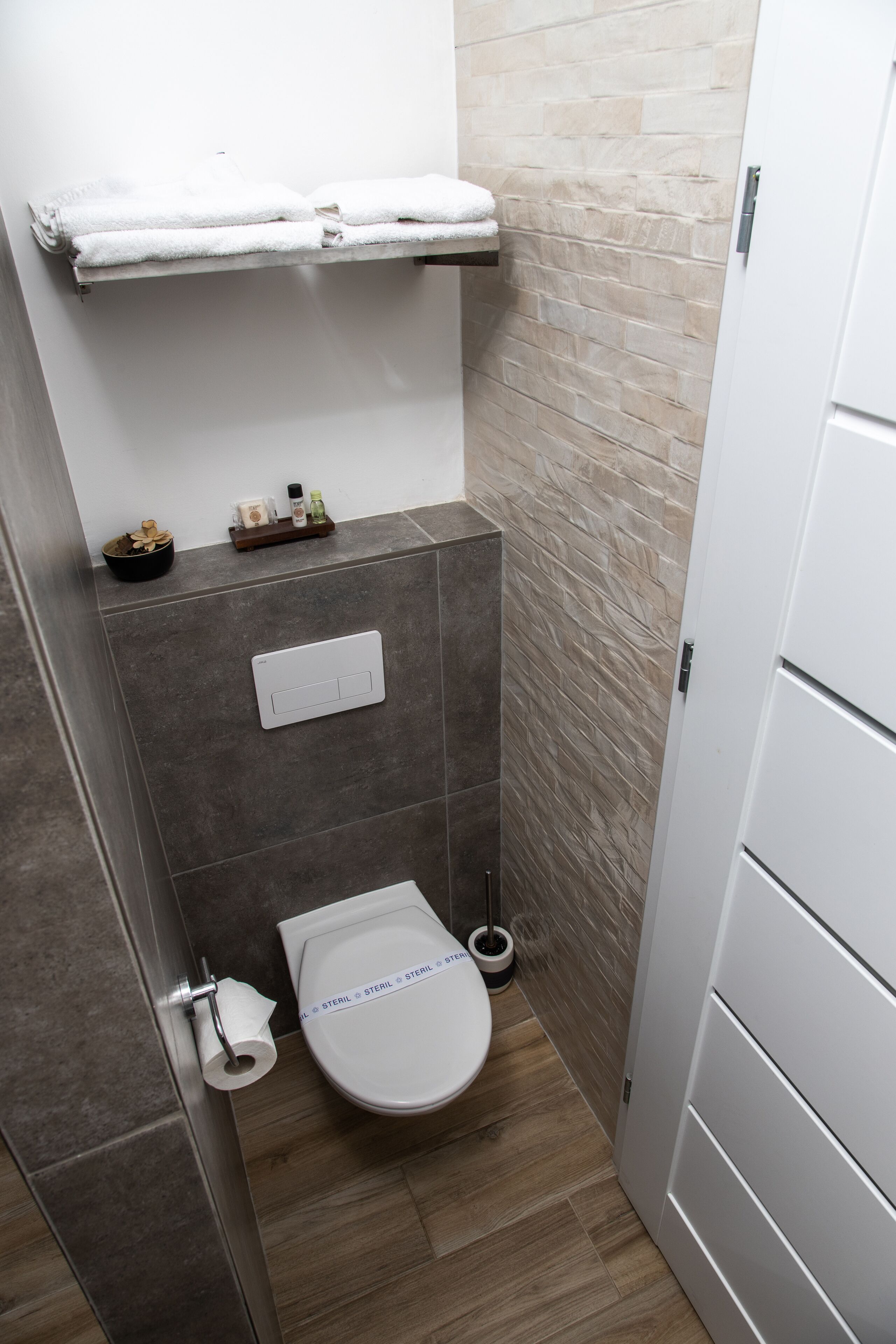 A small bathroom with a toilet, a towel rack, and a shelf with toiletries.