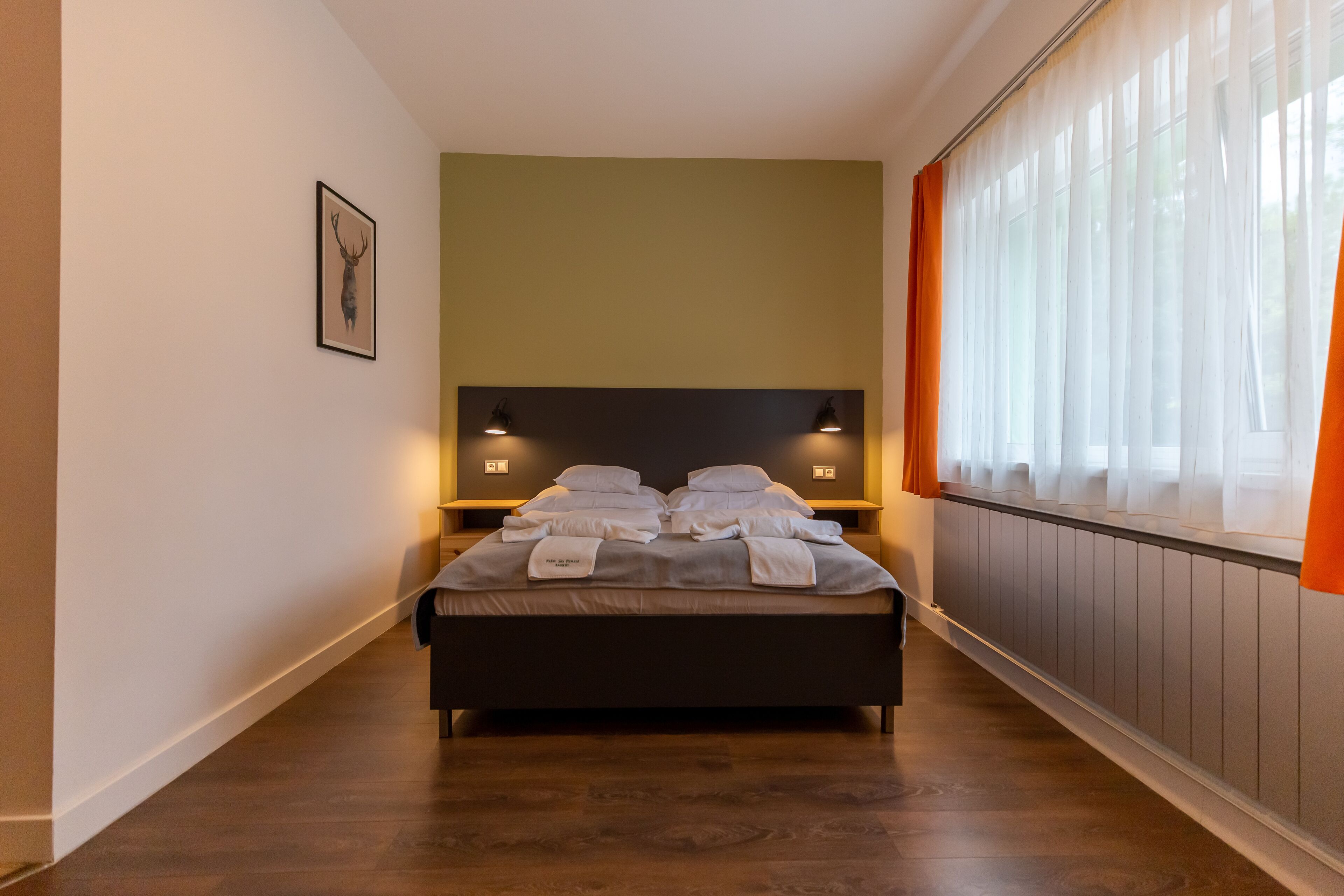 Cama bem arrumada com travesseiros e cobertor, mesa de cabeceira com abajur, quadro na parede e janela com cortinas.