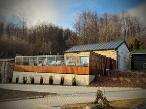A modern building with a glass facade, wooden deck, and stone walls. - Fehér Sas Panzió és Étterem  (Nagyvisnyó)