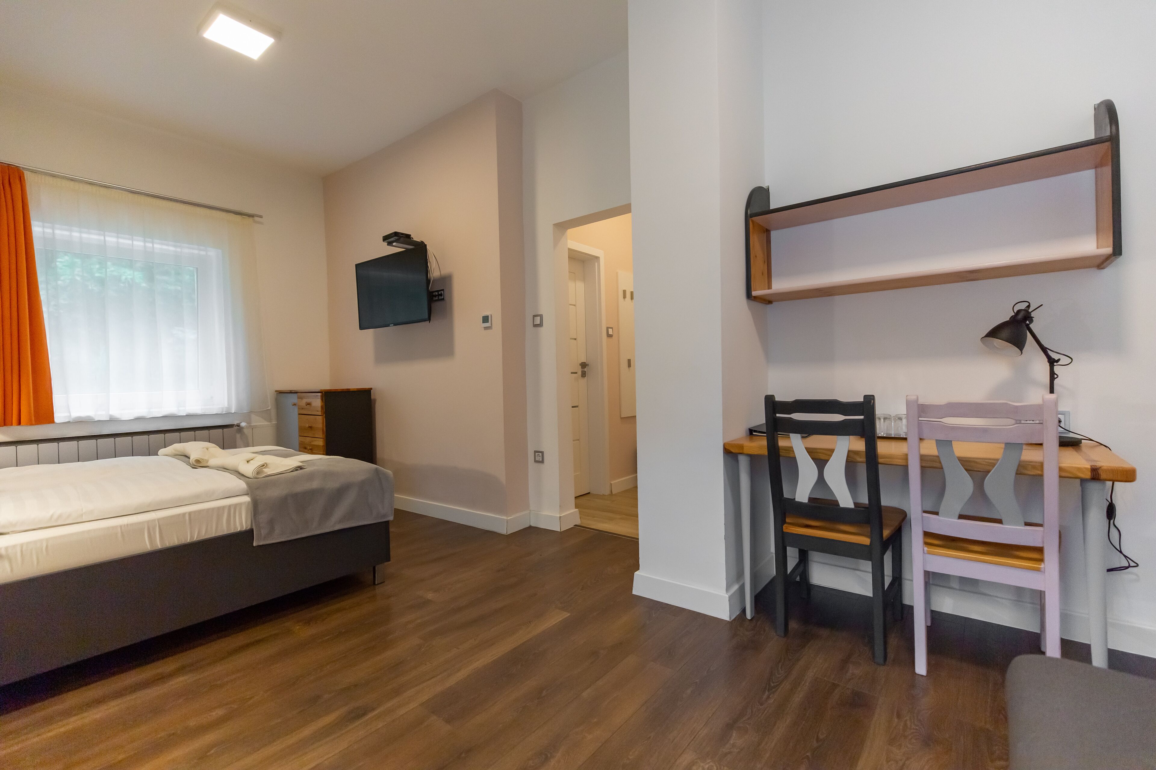 A bedroom with a bed, a desk with a chair, and a TV mounted on the wall.