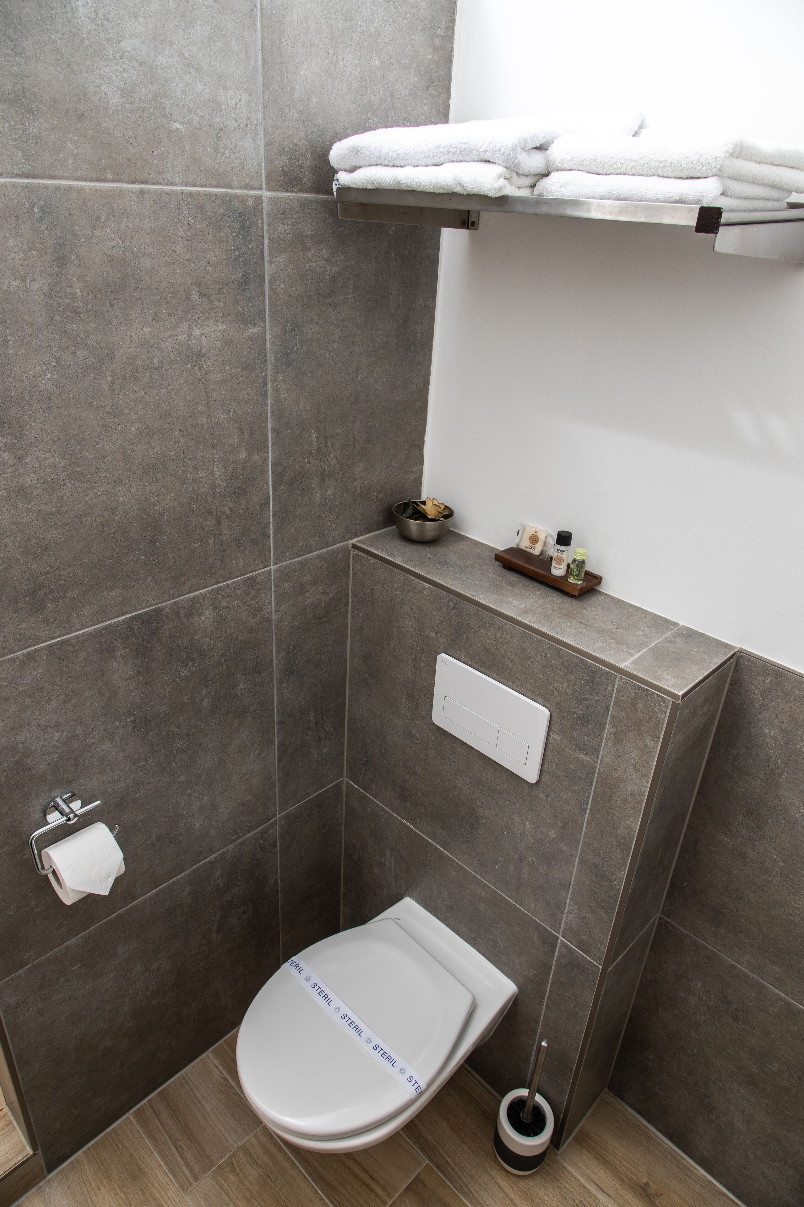 Une salle de bain comprenant des toilettes, un porte-serviettes, une étagère avec des articles de toilette et un support à papier toilette.