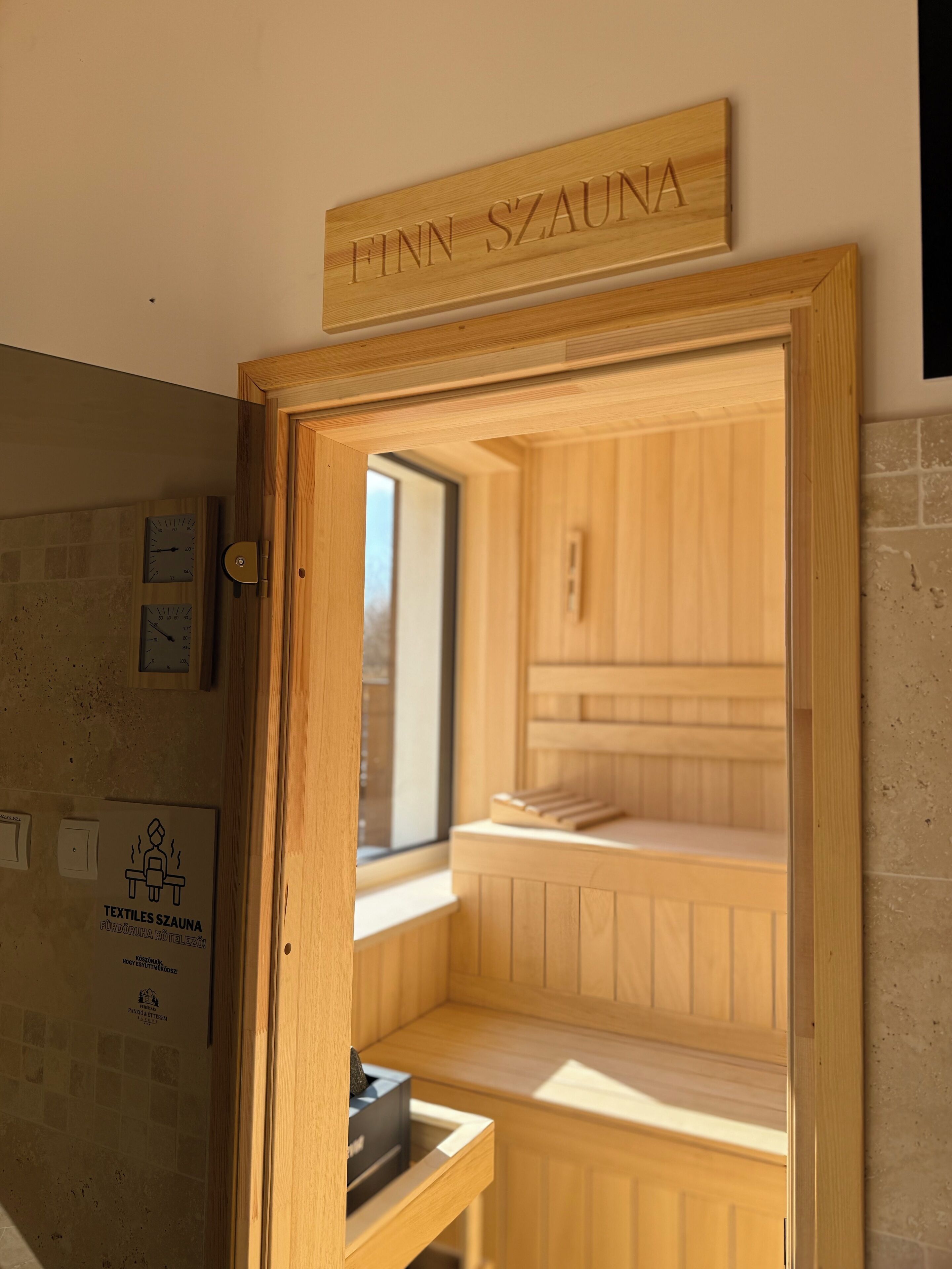Una sala de sauna con paredes de madera y un banco. Hay un cartel sobre la puerta que dice 'FINN SZAUNA'.