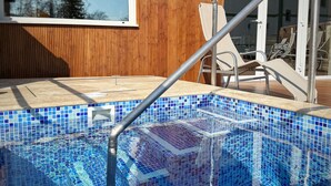 Una piscina con mosaicos, una escalera metálica y sillas de descanso.