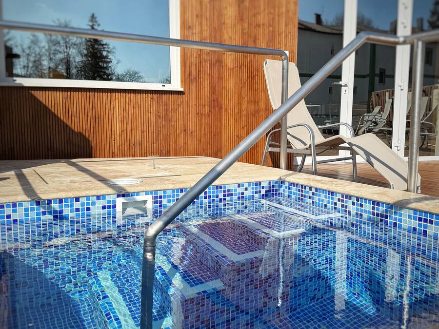 A swimming pool with mosaic tiles, a metal ladder, and lounge chairs.