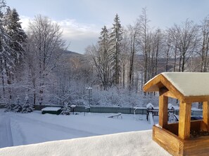 A wooden bench in a snowy landscape with a fence and trees in the background. - Fehér Sas Panzió és Étterem  (Nagyvisnyó)