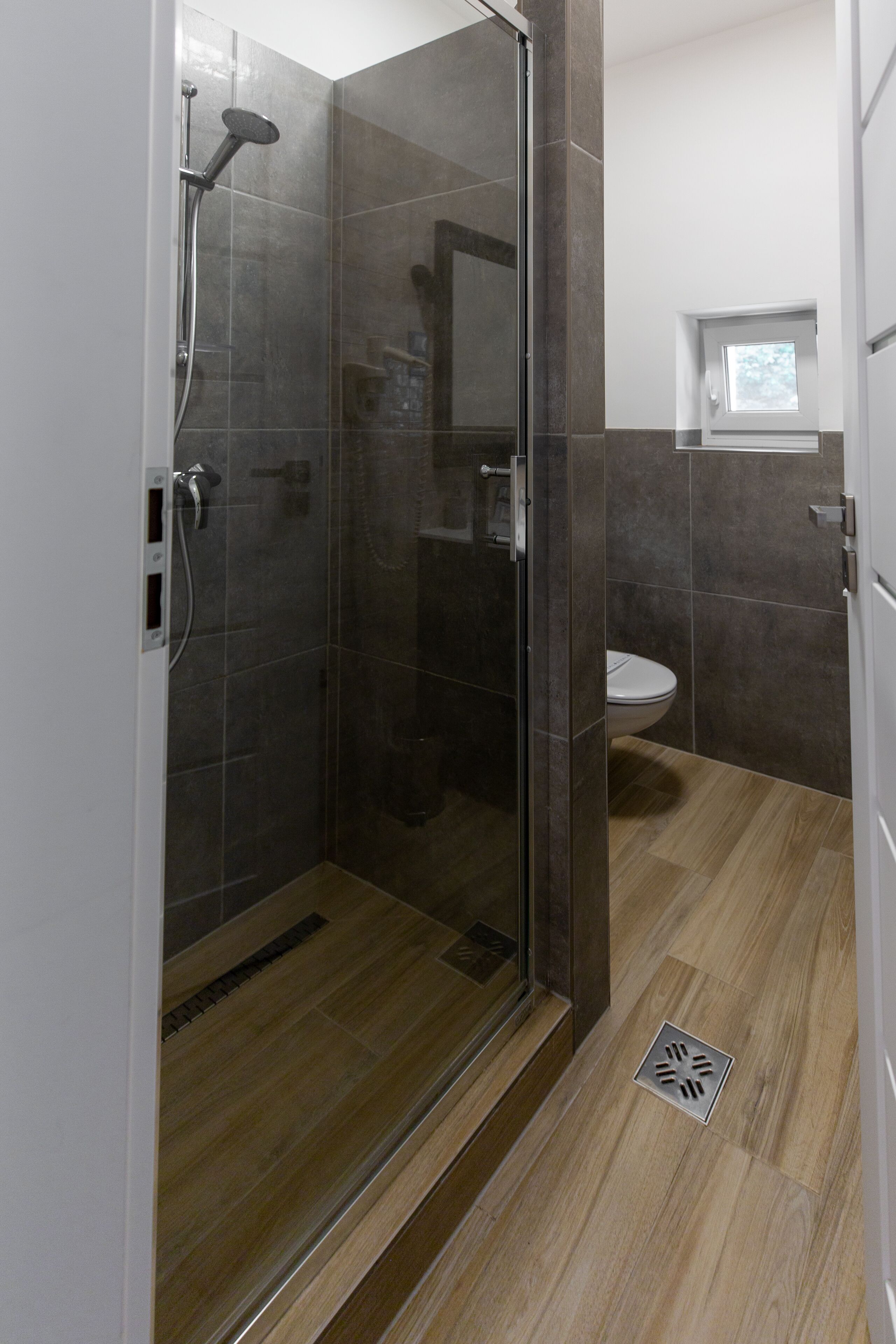 Un baño moderno con ducha envuelta en vidrio, inodoro y ventana sobre el lavamanos.