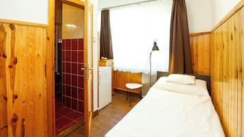 A hotel room with a wooden wardrobe, a small kitchenette, a bed with white linens, and a window with curtains.