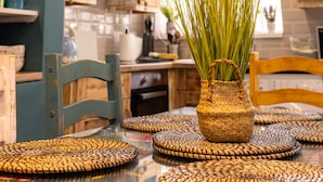 A kitchen with a woven basket containing green plants, wooden chairs, and woven placemats on a glass table. - James' Place @ The Park (Merthyr Tydfil)