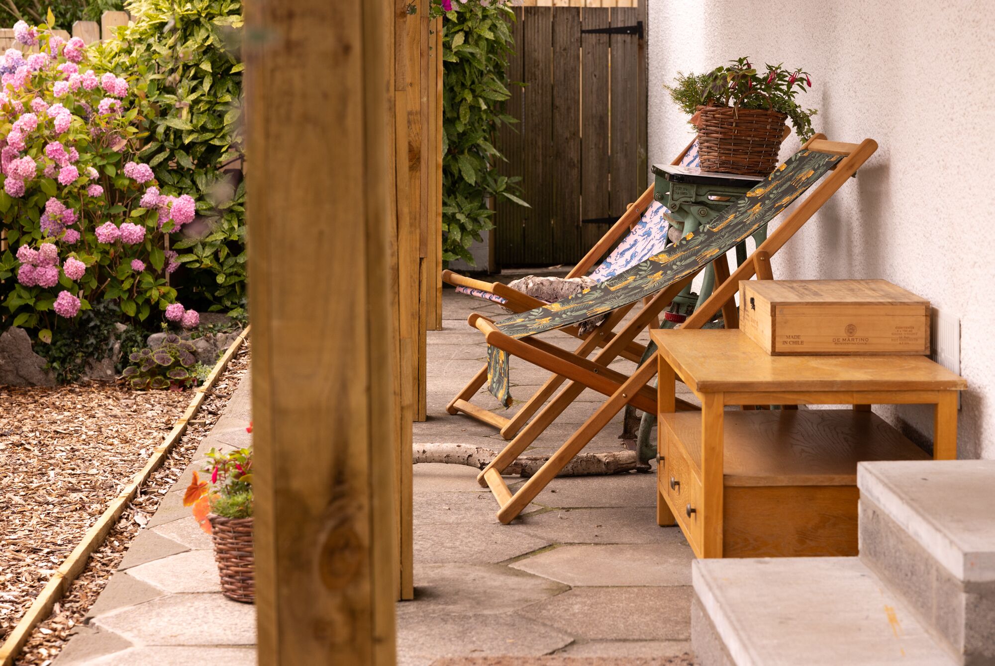 Une terrasse en bois avec un fauteuil suspendu en forme de hamac, une table en bois et une plante en pot.
