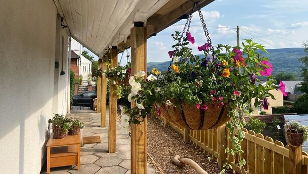A covered outdoor area with hanging flower baskets and a wooden fence. - James' Place @ The Park (Merthyr Tydfil)