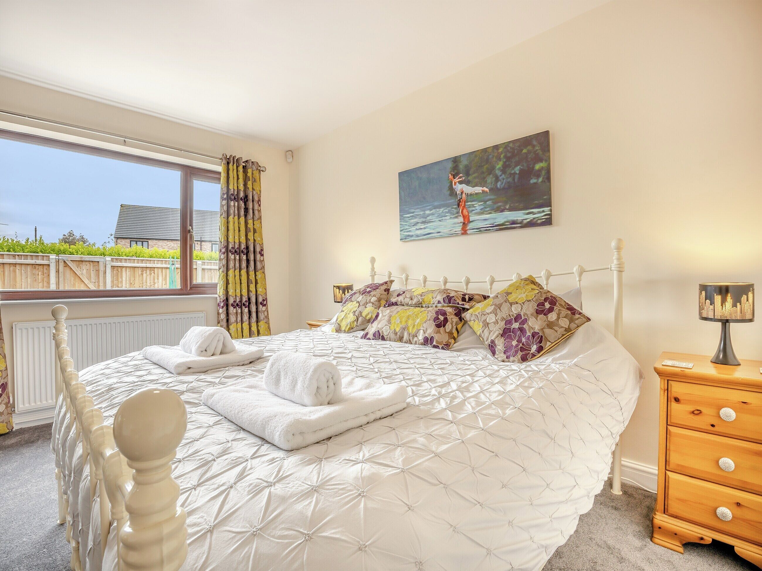 A bedroom with a large bed, a painting on the wall, and a window with curtains.