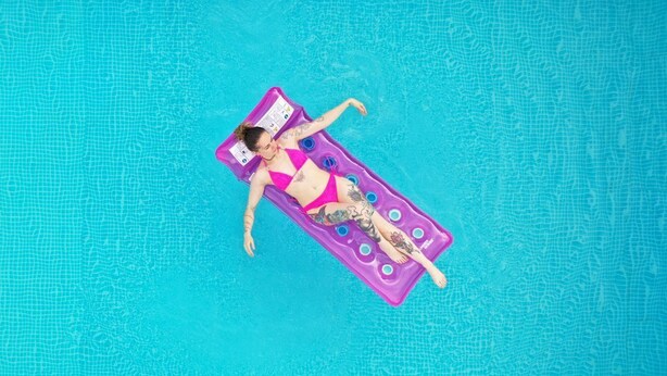 Uma pessoa deitada em um boião roxo numa piscina azul cristalina.