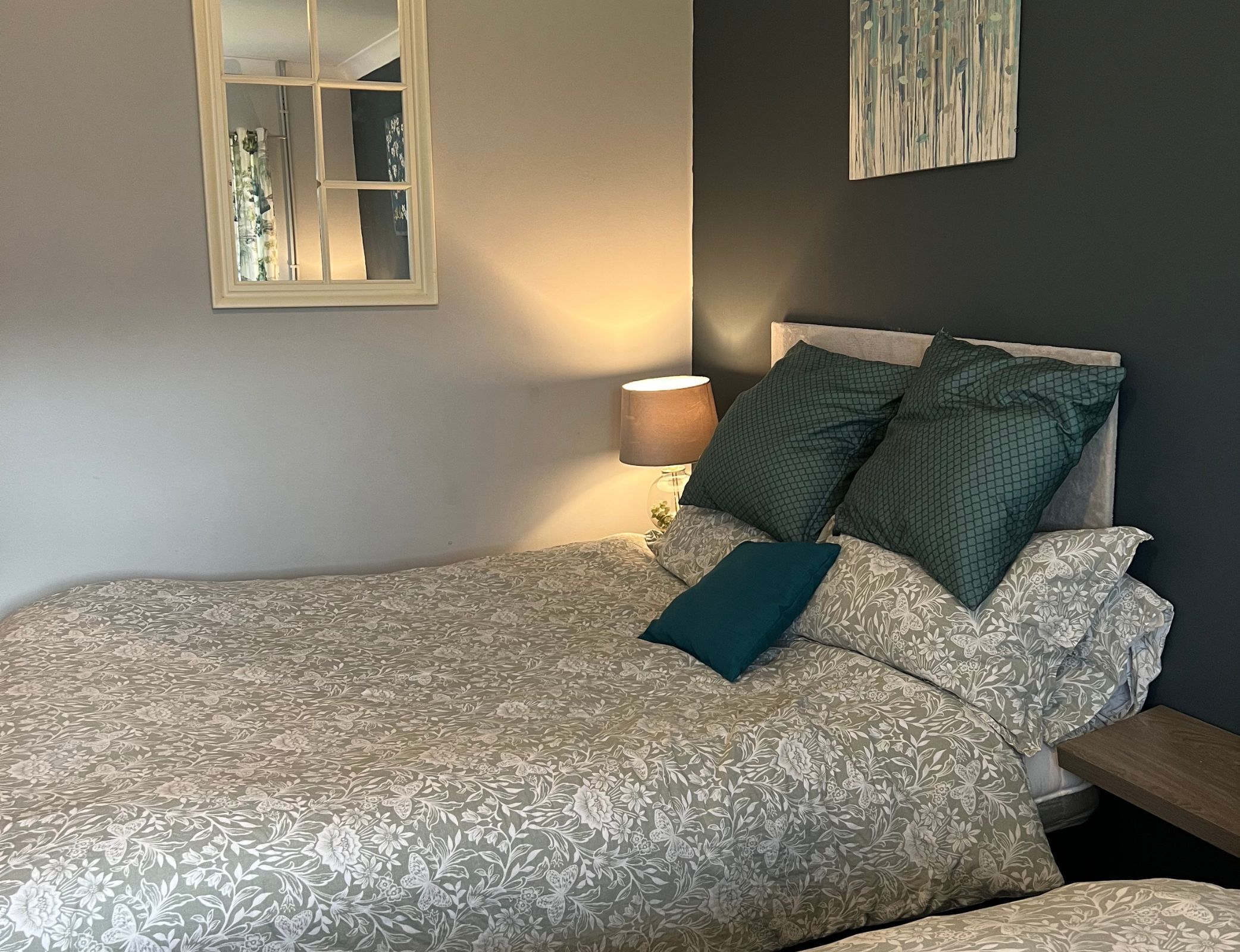 Un dormitorio con cama, mesita de noche, lámpara y espejo.