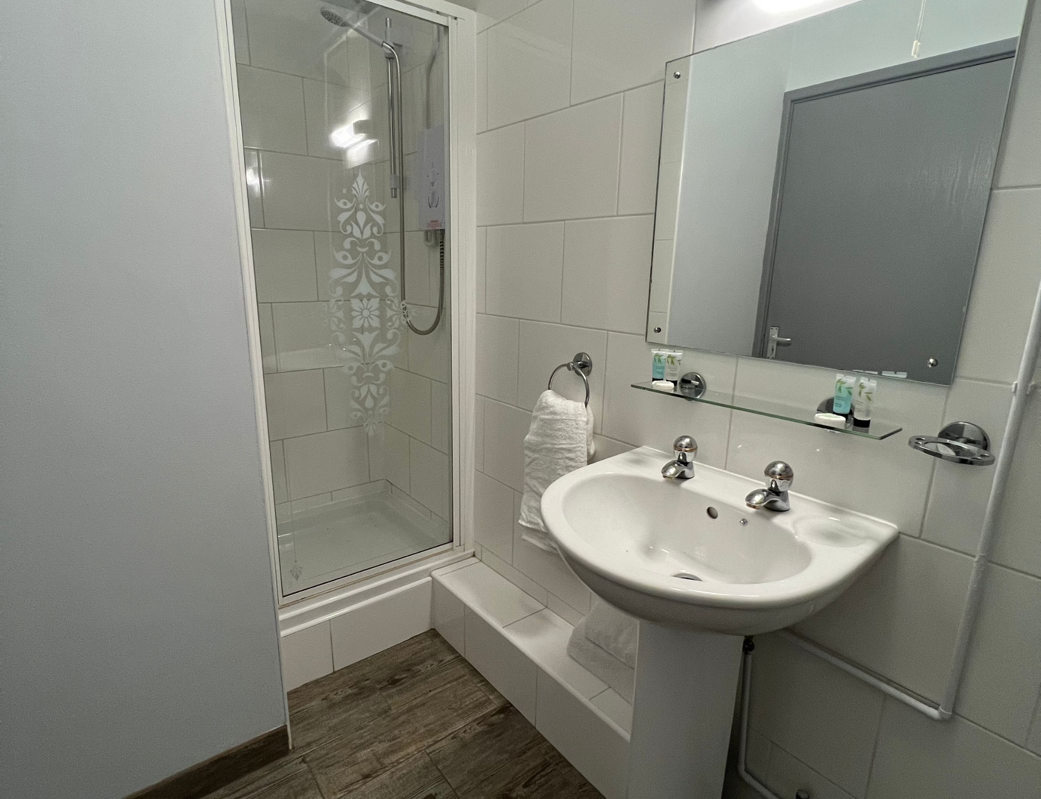 Een moderne badkamer met een douchecabine van glas, een witte wastafel en een spiegel boven de wastafel.