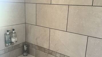 Un baño con lavamanos, dos dispensadores de jabón para manos y una zona de ducha con azulejos color beige.