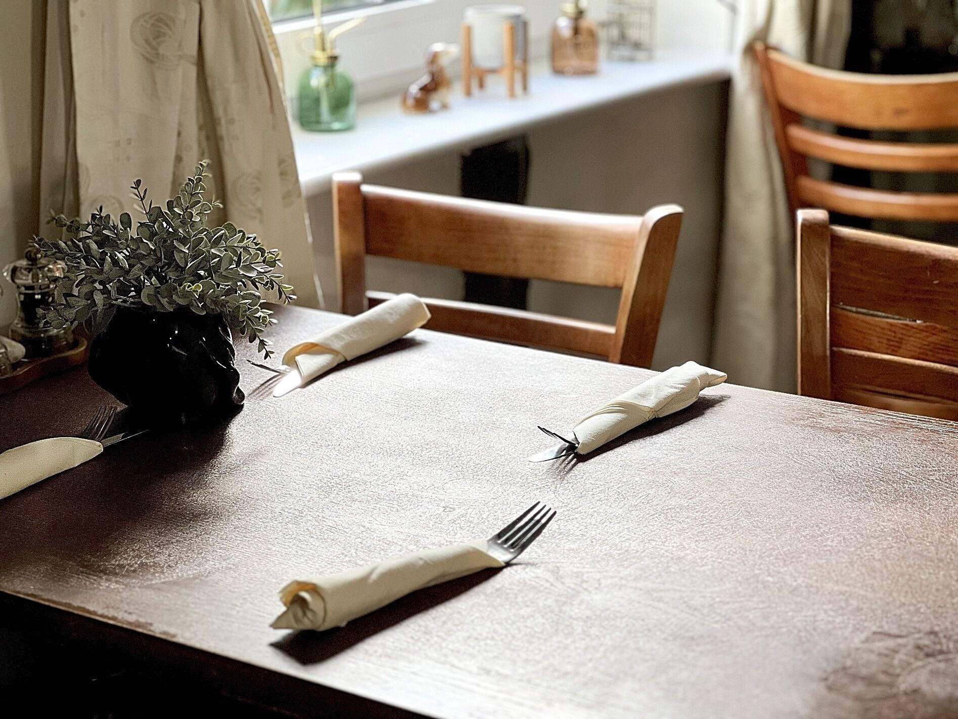 A dining table with a vase of green foliage, a folded napkin, and a fork.