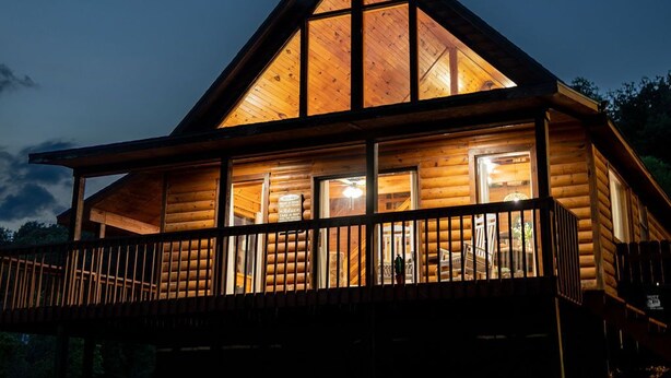 A log cabin with a balcony and large windows, surrounded by a gravel area.