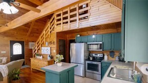 A cozy cabin interior with a wooden staircase, a kitchen with teal cabinets, and a dining area with a wooden table and chairs.