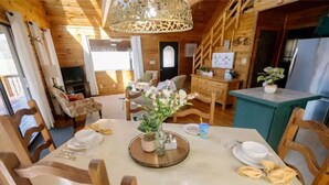 A wooden cabin interior with a dining table set for four, a staircase, and a kitchen area.