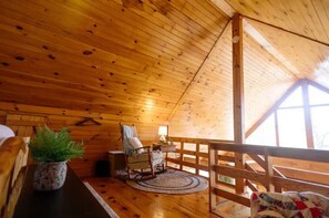 Relax in this cabin with a wooden rocking chair, potted plant, and a view from the window.