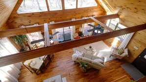 A high-ceilinged wooden cabin with a dining area, sofa, and a view of the outdoors.