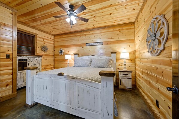 Un dormitorio de cabaña de madera con una cama, un ventilador de techo, un cartel que dice "HOCHATOWN, OK" y un adorno de pared.