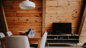 Puupaneloitu huone, jossa on ruokapöytä, tuoleja, televisio ja valkoinen riippuvalaisin.