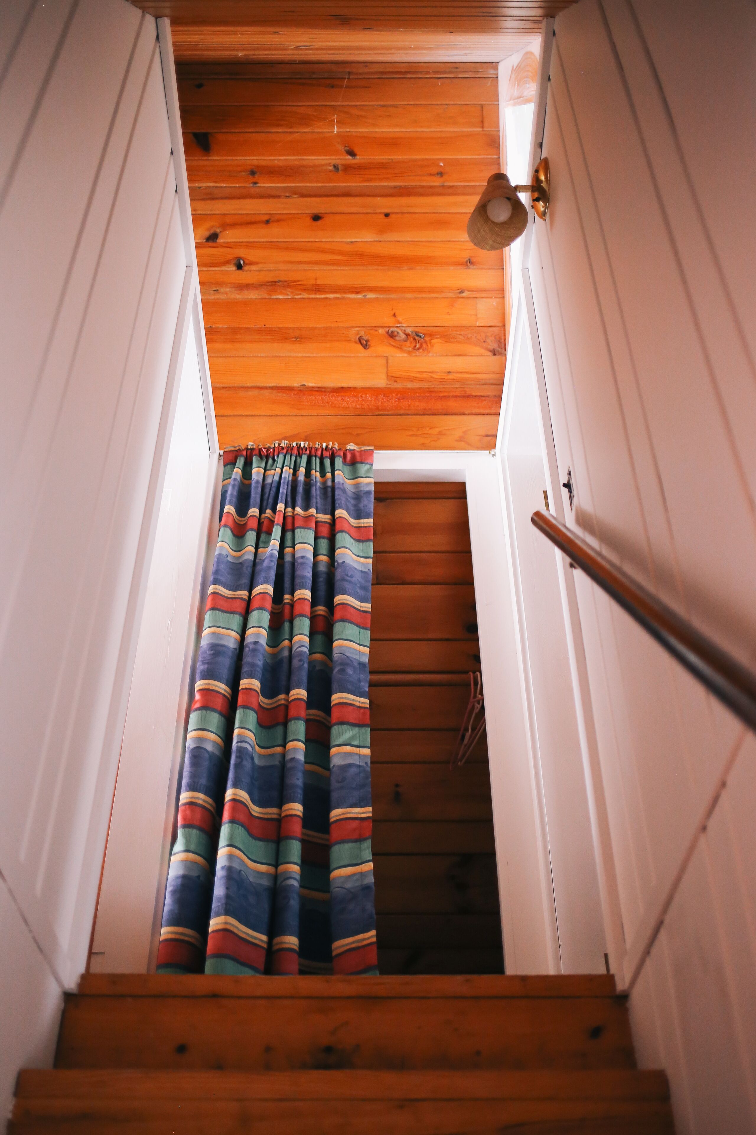 A wooden staircase with a striped curtain and a metal handrail.