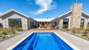 Ett modernt hus med en swimmingpool, en fasad av sten och en uteplats med solstolar.