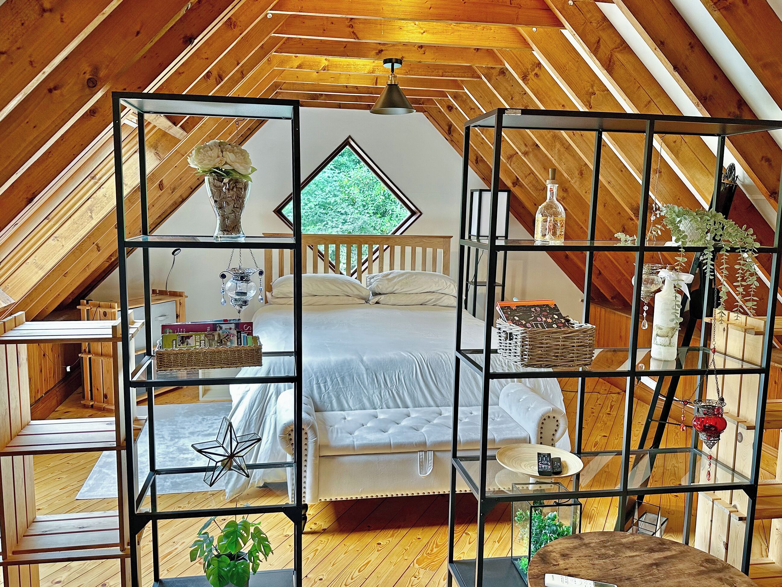 Ein gemütliches Schlafzimmer im Dachgeschoss mit Bett, Regalen und Blick ins Grüne.