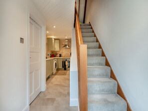 Un couloir étroit mène à une cuisine où se trouve un escalier en bois.