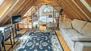 Un dormitorio abrigado en el ático, con cama, televisor, sofá y un tapete decorativo.