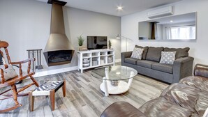Una sala de estar moderna con chimenea, una mesa de centro de vidrio, un sofá y un sillón mecedor.