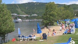 Un complejo turístico junto al lago con sillas de playa, sombrillas y vistas al lago y a las montañas.