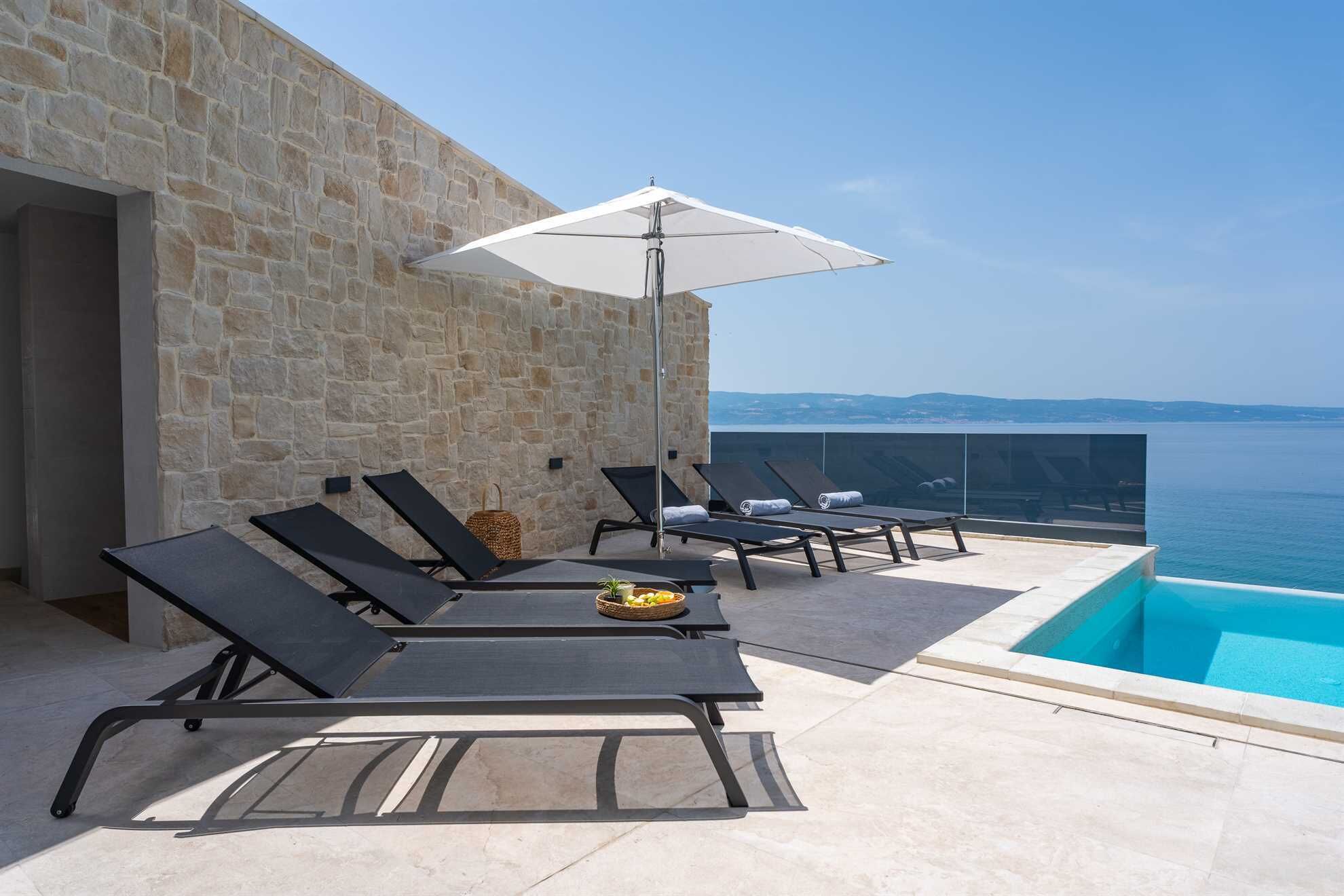A rooftop pool area with lounge chairs and an umbrella, overlooking a body of water.