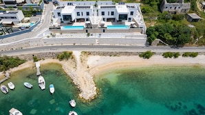 Een moderne villa met een zwembad, boten en een strand.