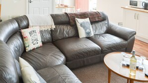 Ein Wohnzimmer mit einer Ledersofa, einem runden Couchtisch und einer Weinflasche.