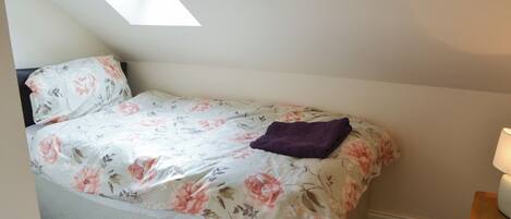 Una cama individual con una colcha estampada y un edredón púrpura, con un tragaluz arriba.