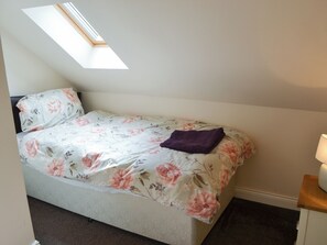 Ein Einzelbett mit blumigem Überwurf, einer violetten Decke und einem Oberlicht darüber.