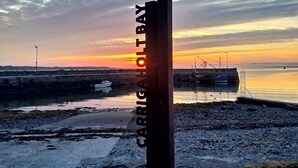 A sunset view at Carrigtain Bay with boats docked and a rocky shoreline.